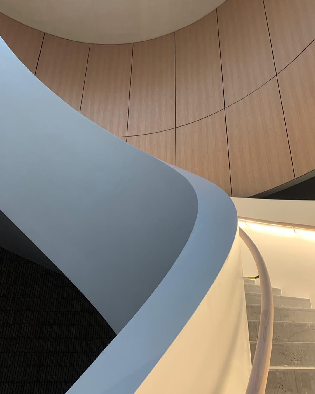 The curved underside of the same staircase sweeping past a timber-lined ceiling above a pale stone stair