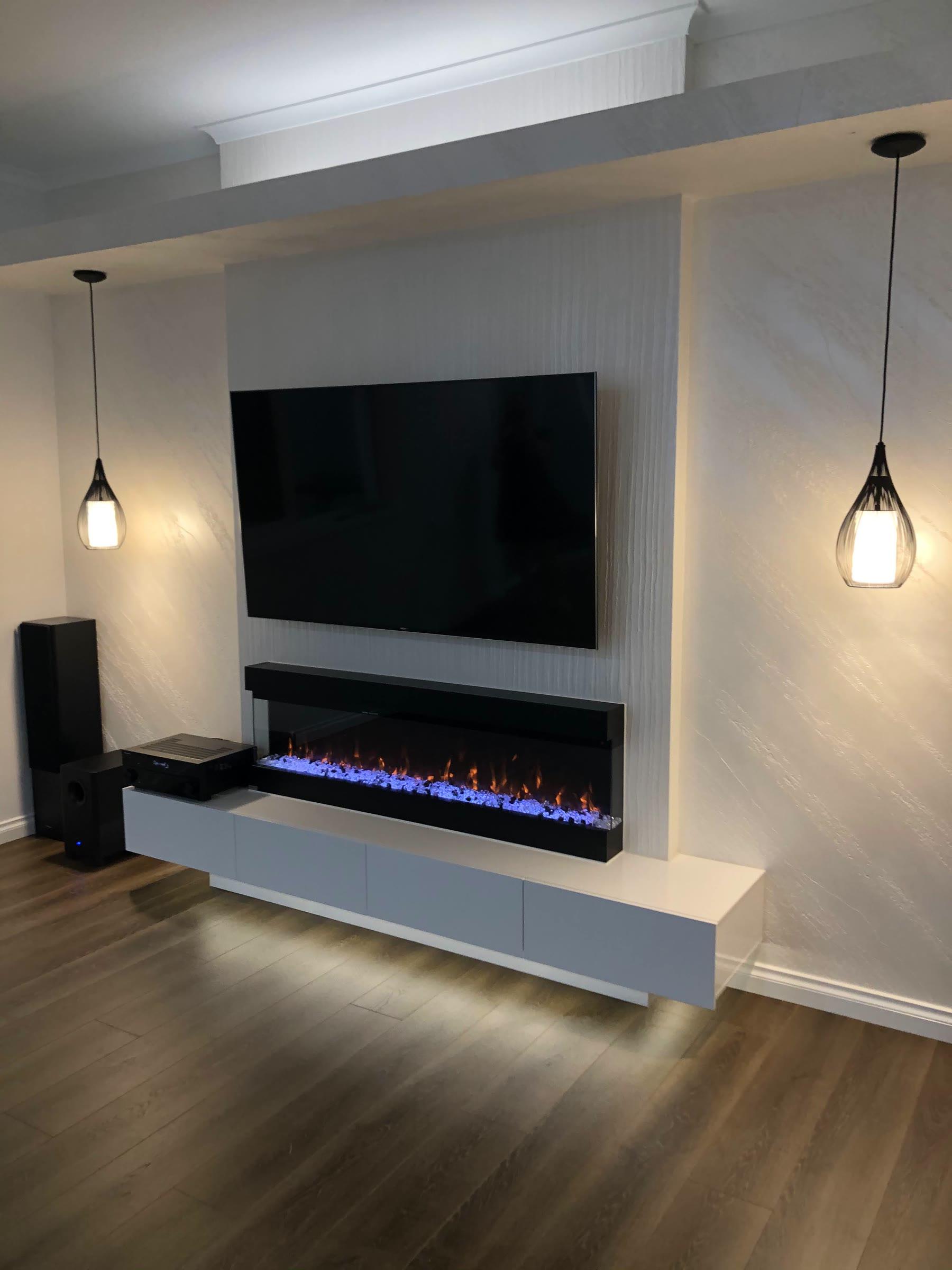A media wall finished in pale vertically textured plaster, a mounted television above a long electric fire and a white floating cabinet, glass pendants either side over a timber floor
