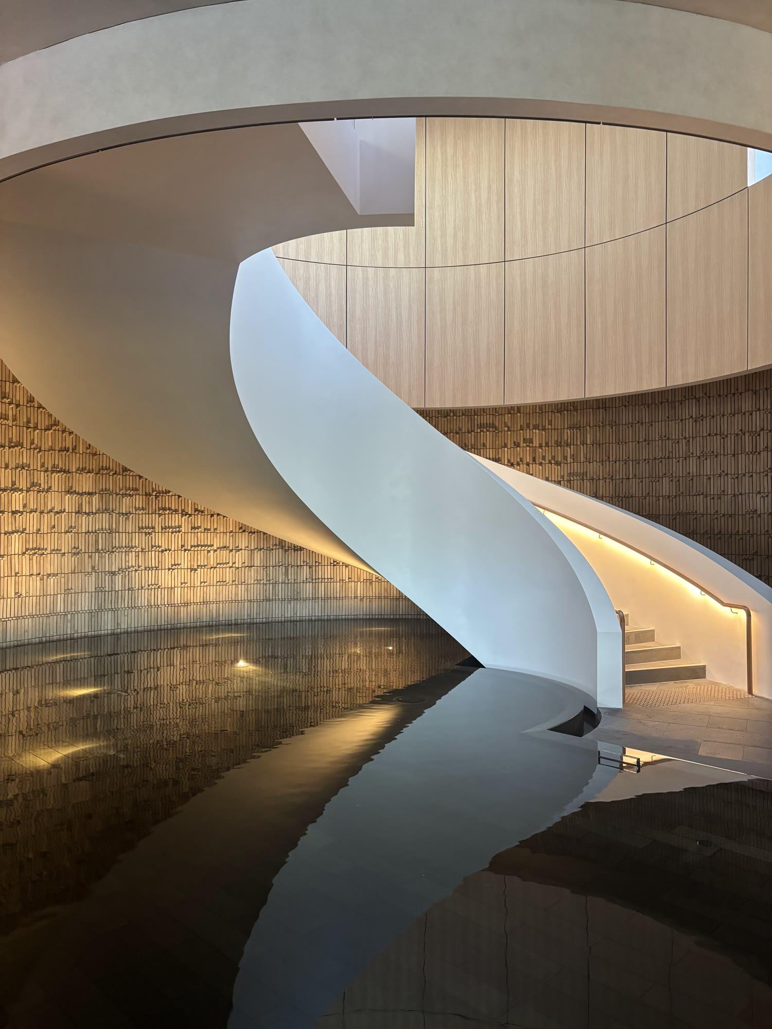 A sculptural white curved staircase at Alba Thermal Springs, finished in polished natural white plaster beneath a curved timber-lined ceiling